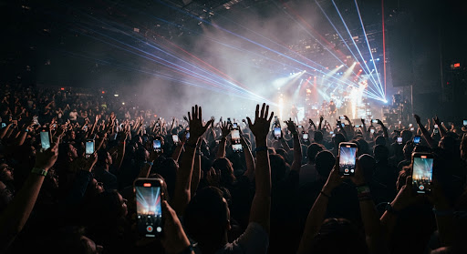 Concert audience crowd hands in the air with illuminated smartphones and laser beams cutting through venue haze